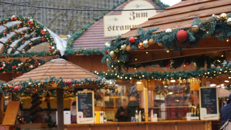 A blurry picture of wooden Christmas huts adorned with Christmas garlands with baubles and fairy lights.