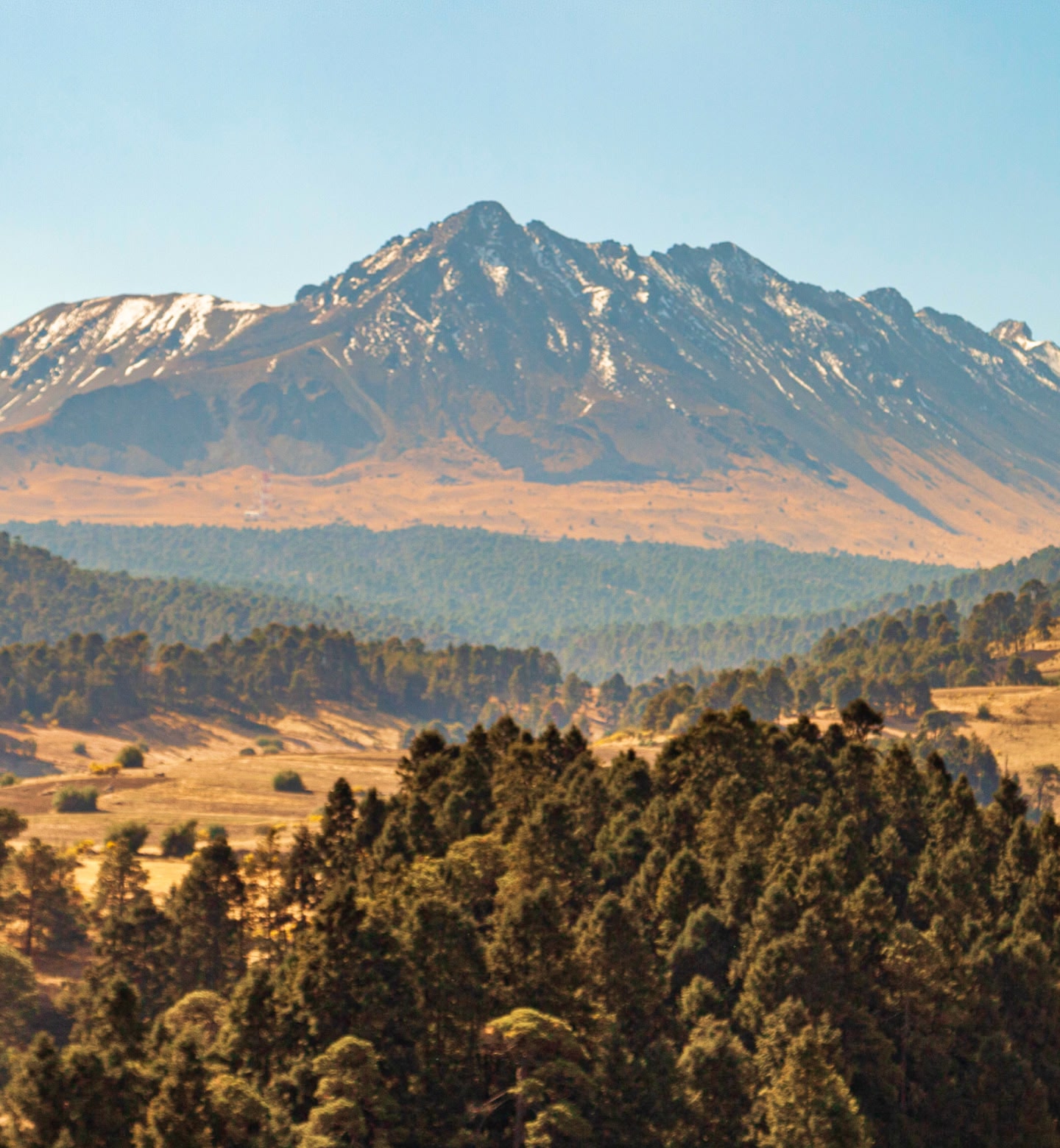 Une montagne enneigée s'élève au-dessus de collines boisées baignées d'une lumière dorée à Toluca, au Mexique.