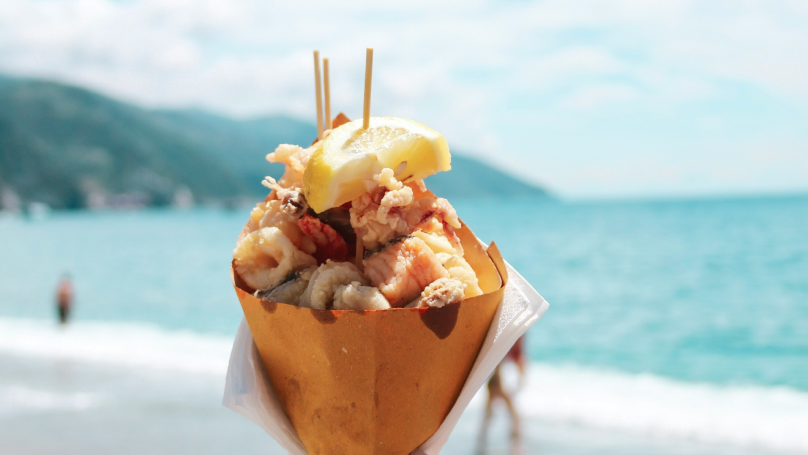 A person holding up a cone with some typical food from Naples on the beach