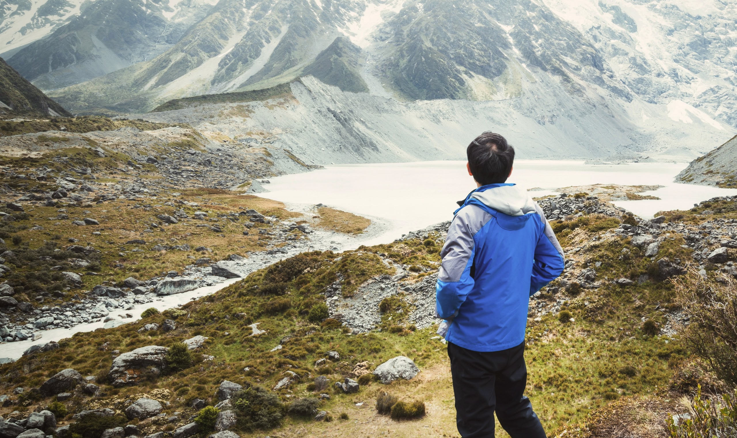 A man in a blue jacket looks out over a snow-dusted mountain landscape.
