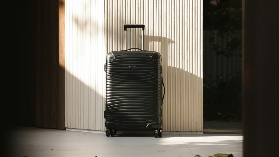 A black suit case resting against a white wall
