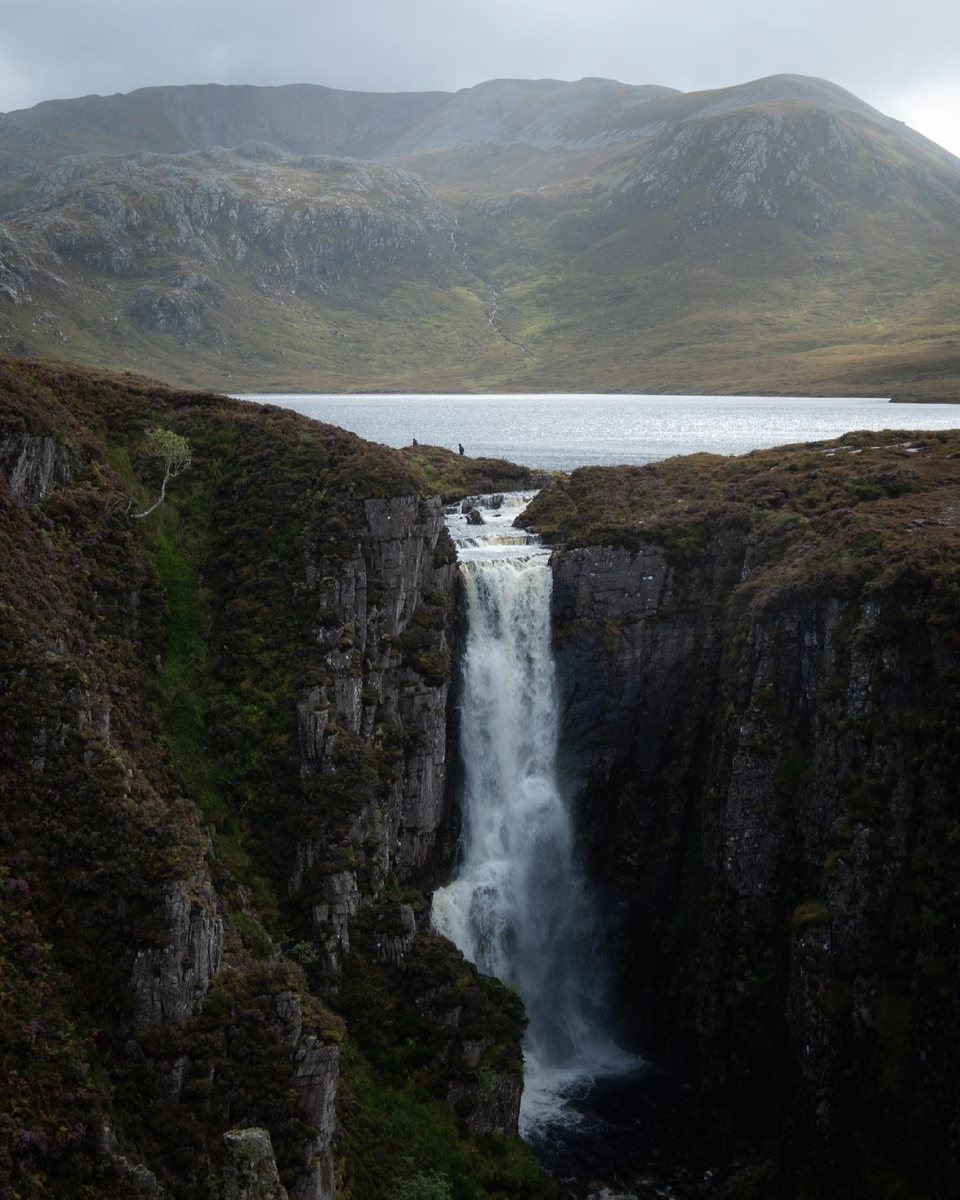 Vaccinated travelers in the UK walk the rim of a cliff. A waterfall rushes off of the side.