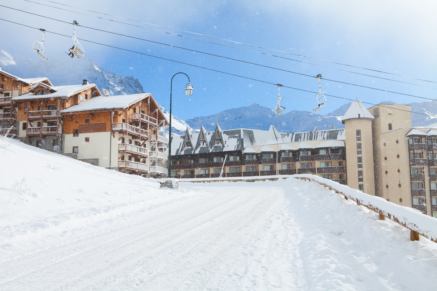 View of a chalet hotel with a ski lift running past it and a snowy road in the foreground