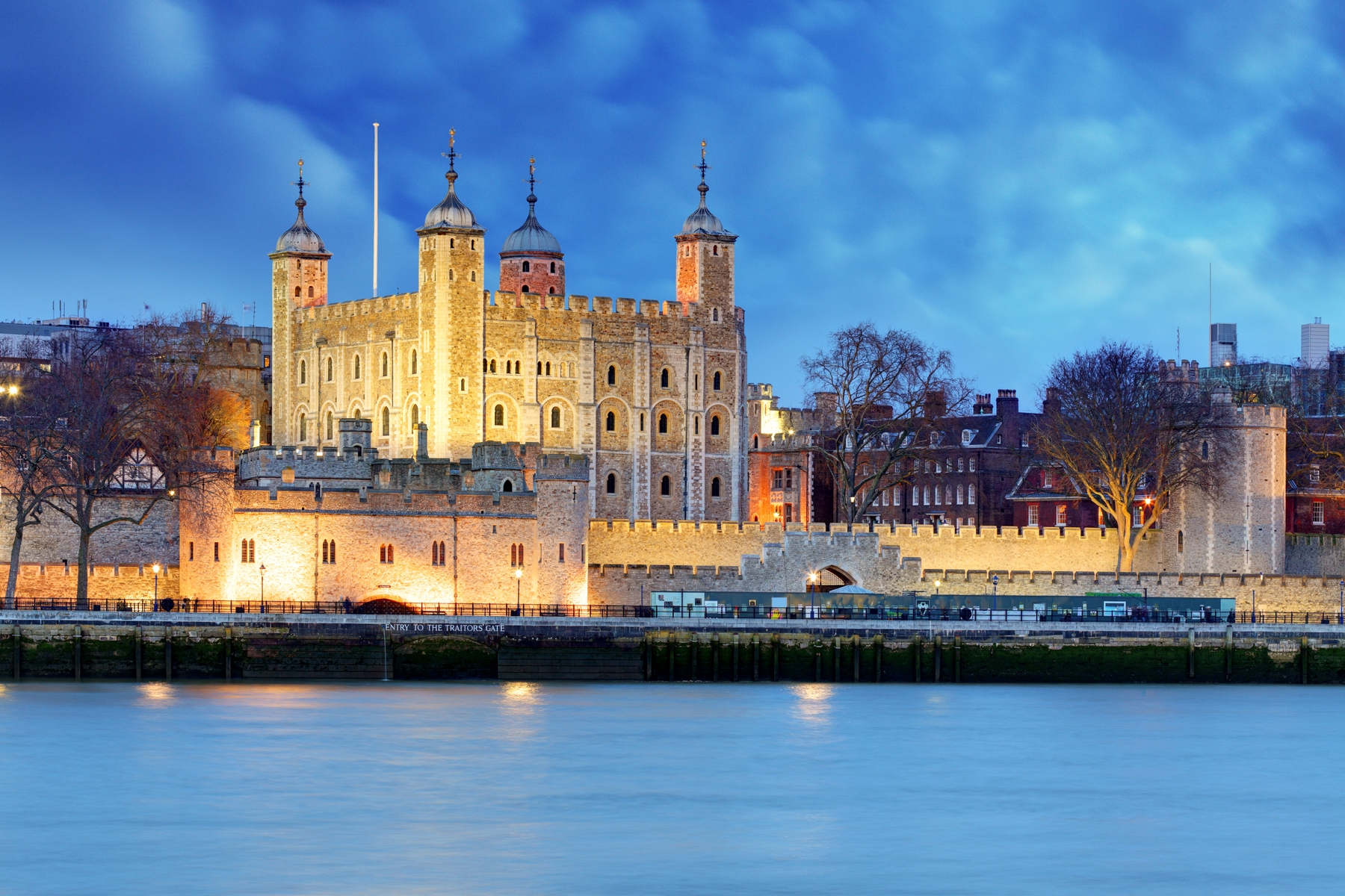 The Tower of London by evening, lit brightly against a cloudy backdrop