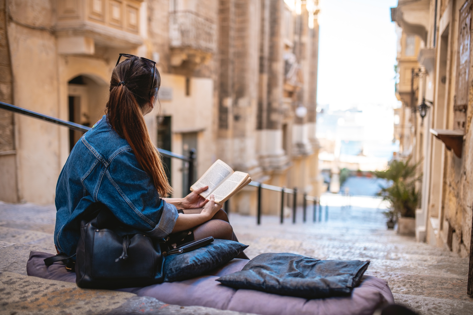 Jeune femme lisant un livre à l'extérieur, sur un escalier, regardant avec nostalgie au loin.