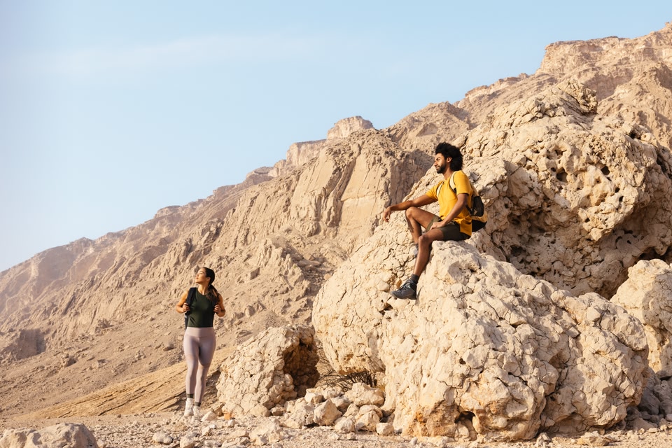 Ein Mann hockt auf einem Felsen, während eine Frau die schroffe Aussicht im Jebel Hafit Desert Park genießt.