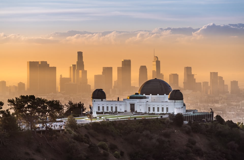 The Griffith Observatory sits on a hill overlooking the hazy Los Angeles skyline during a golden sunset.