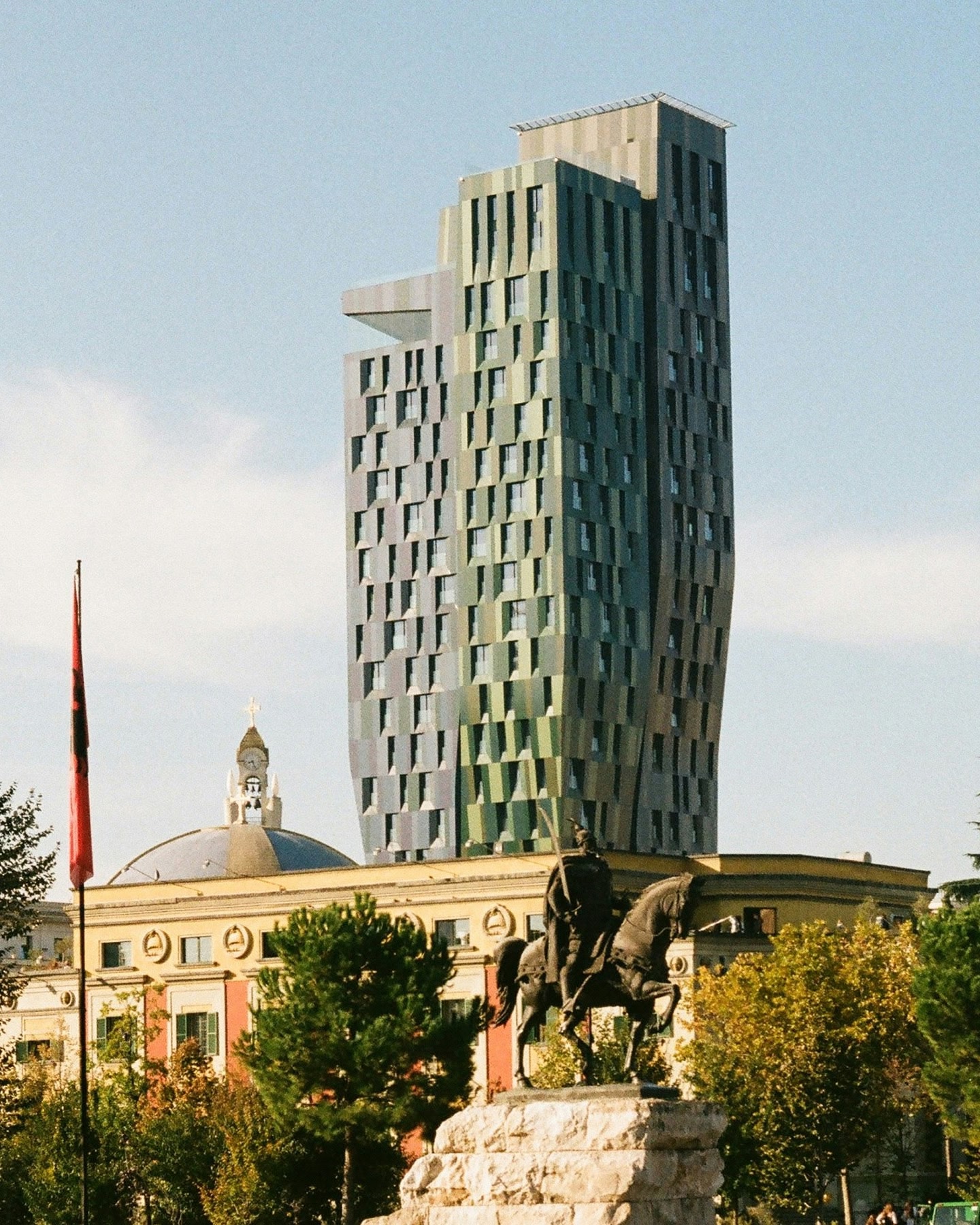 Nowoczesny zielony wieżowiec stojący obok zabytkowego budynku z posągami w Tiranie w Albanii.