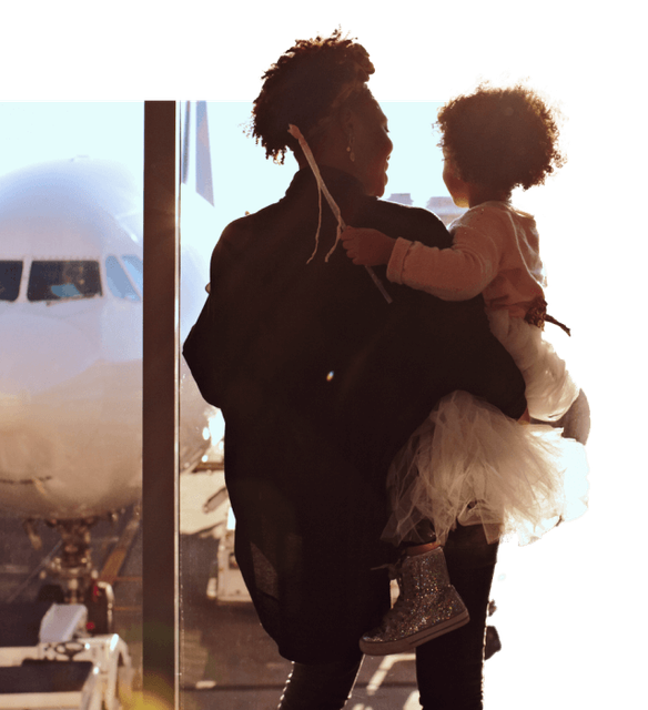 Adult holding a child looking out of a window at an airport.