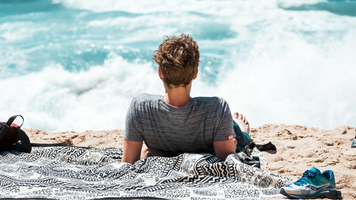 Um homem relaxando na praia olhando para o mar