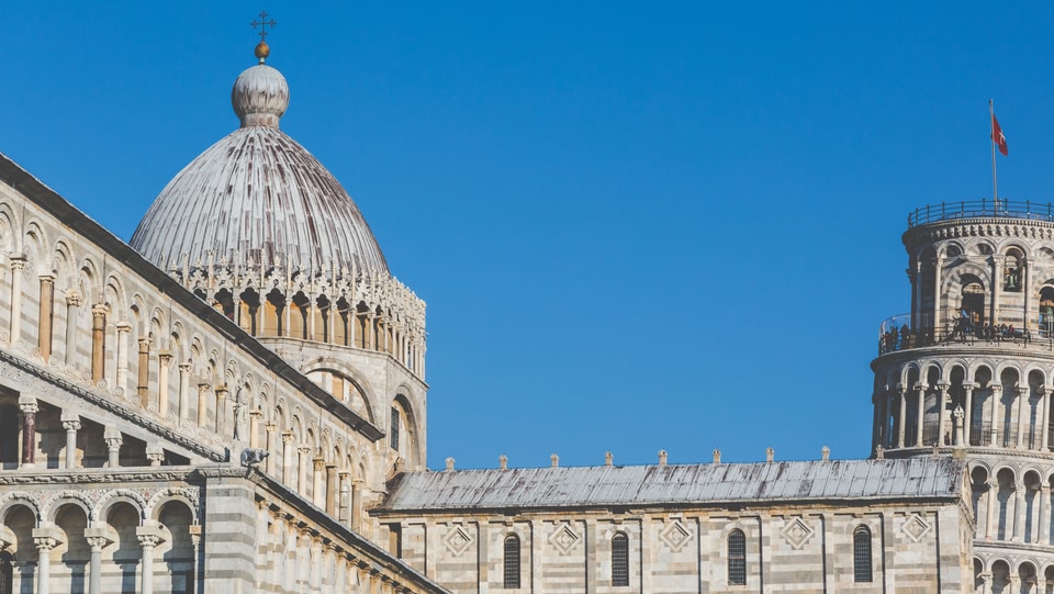 Vista della Cattedrale di Santa Maria Assunta a Pisa, con la sua cupola e una parte della Torre Pendente, sotto un cielo azzurro limpido.