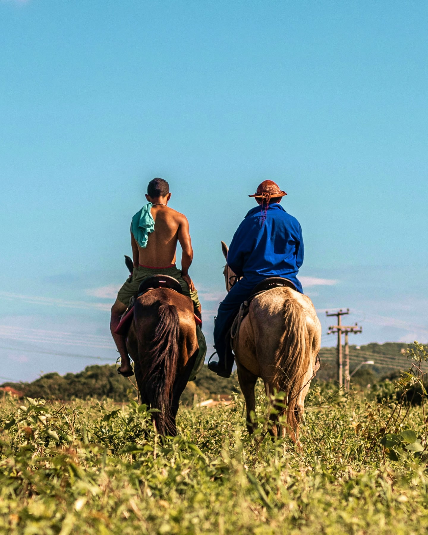 Dois homens cavalgam por um campo verde sob o céu azul em Barretos, Brasil.