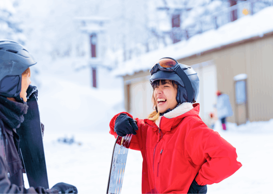 A woman at the bottom of a ski slope leaning on her snow board and laughing with her friend