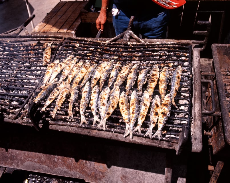 Fresh sardines grilling on a barbecue, a Portuguese delicacy.