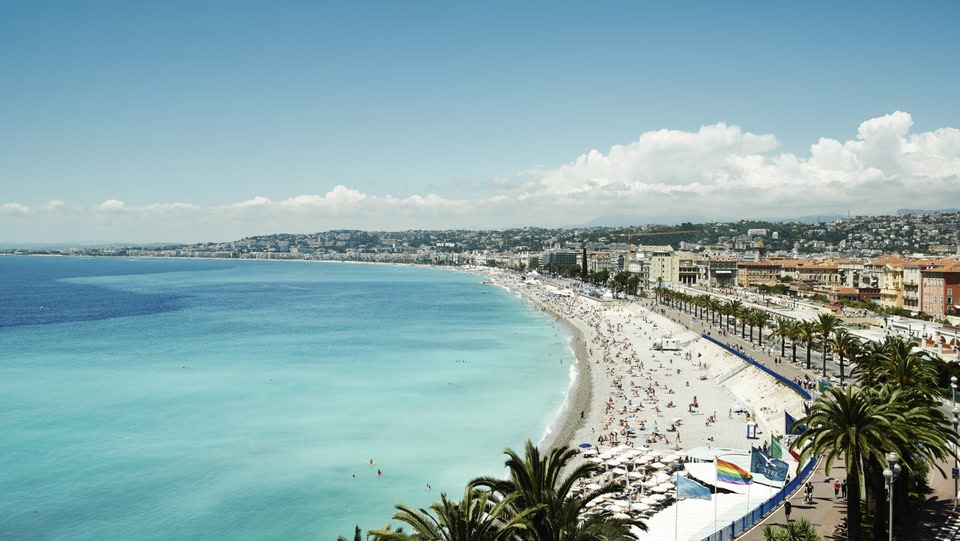 Una spiaggia affollata a Nizza, Francia, con acqua turchese e palme.