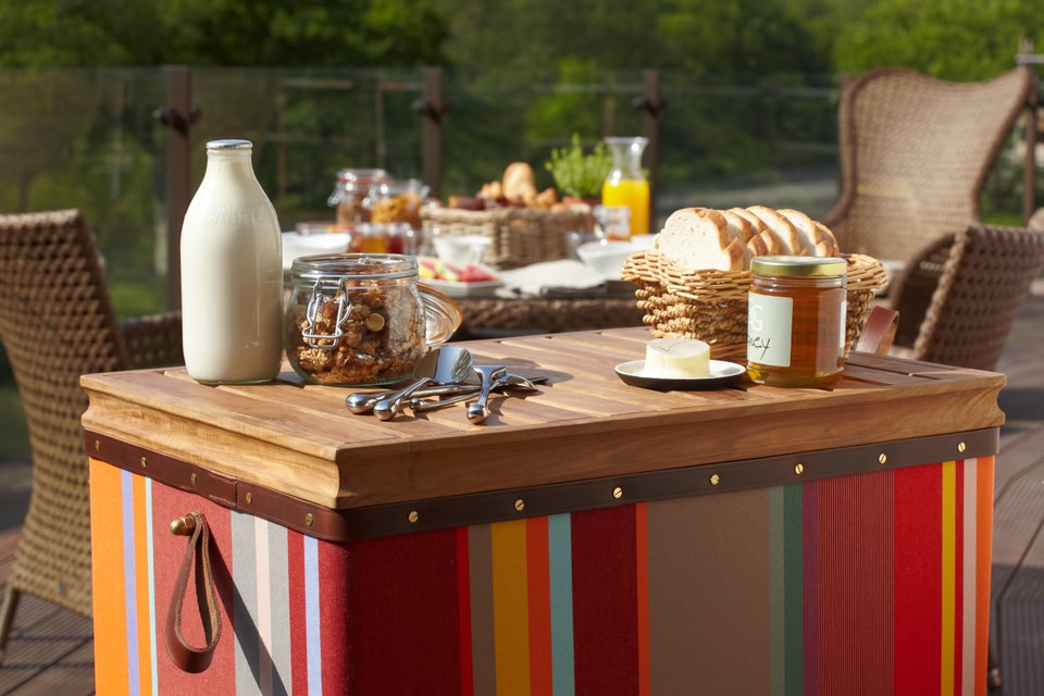 Al-fresco breakfast at Chewton Glen: a glass bottle of milk, granola, honey and fresh bread sitting on a multicoloured hamper, while in the background is a table laden with more bread and a carafe of orange juice.