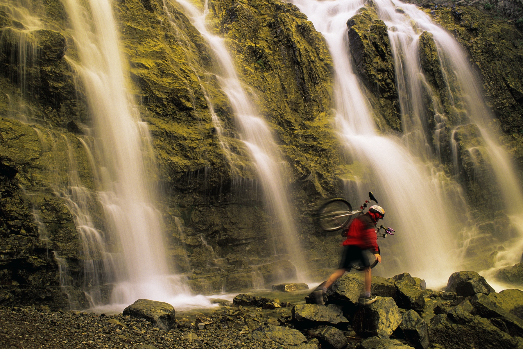 mountain biker holding his bike while hiking near a waterfall