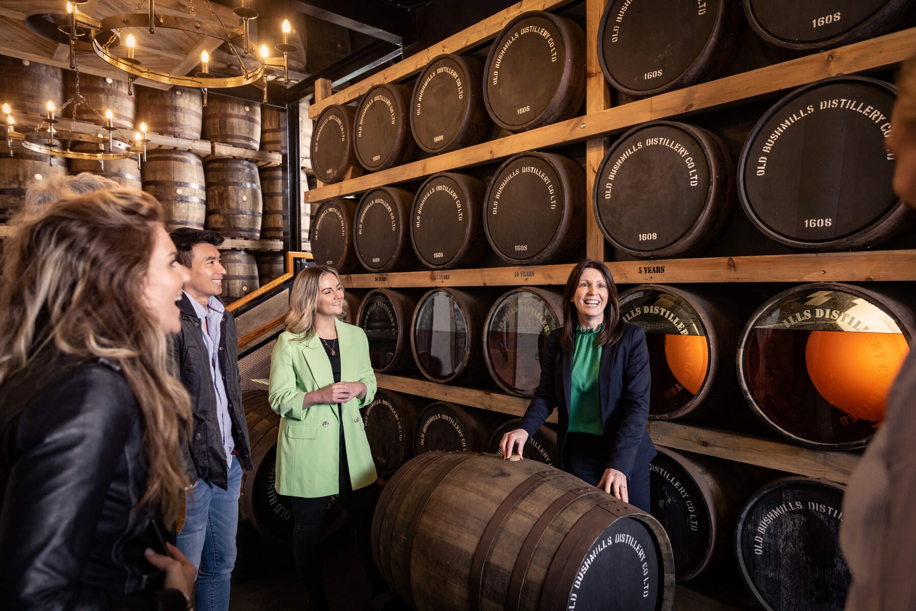 Tour group enjoying a visit to the Bushmills Distillery, while the tour guide talks about the barrels she's surrounded by.