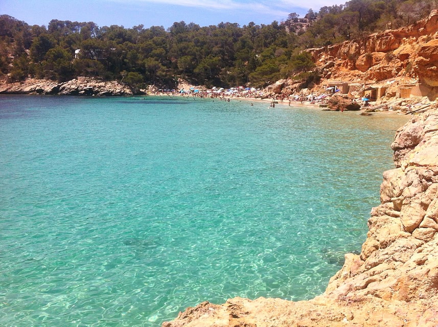 Cala Salada beach in Ibiza, with turquoise waters and sandstone rocks.