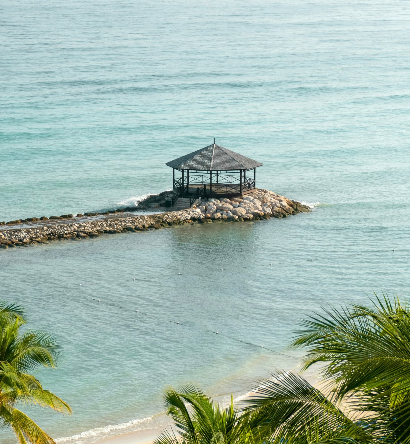 Um quiosque de madeira em um píer rochoso que se estende sobre o mar calmo em Montego Bay, Jamaica.