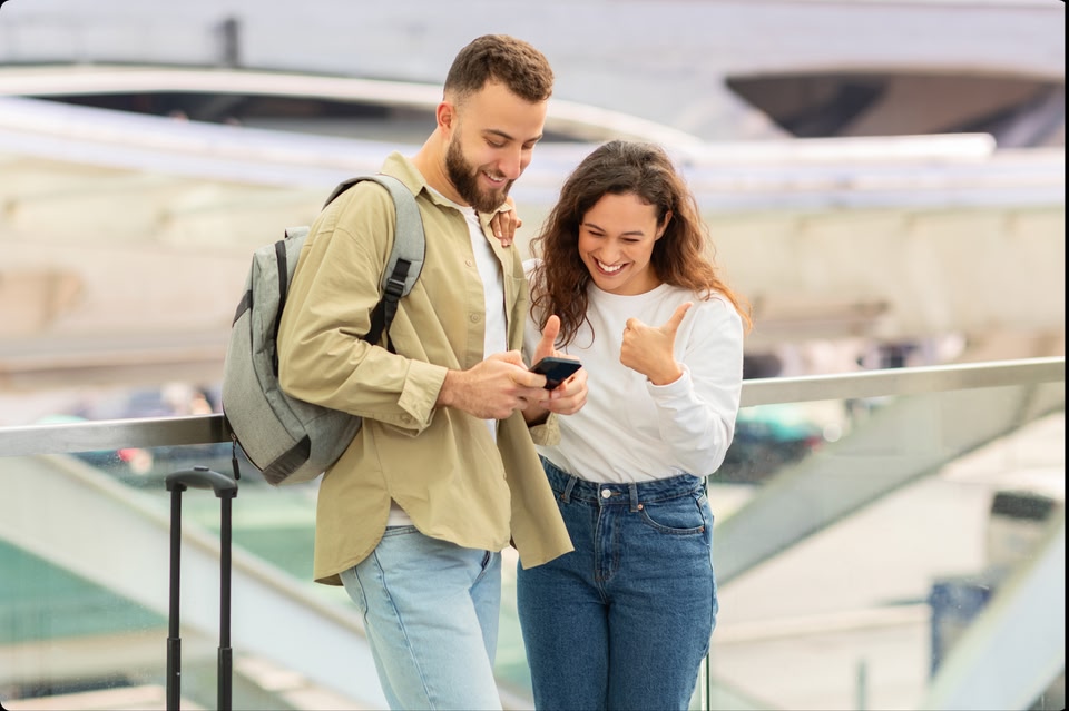 Una pareja parada en un aeropuerto y mirando juntos su teléfono.