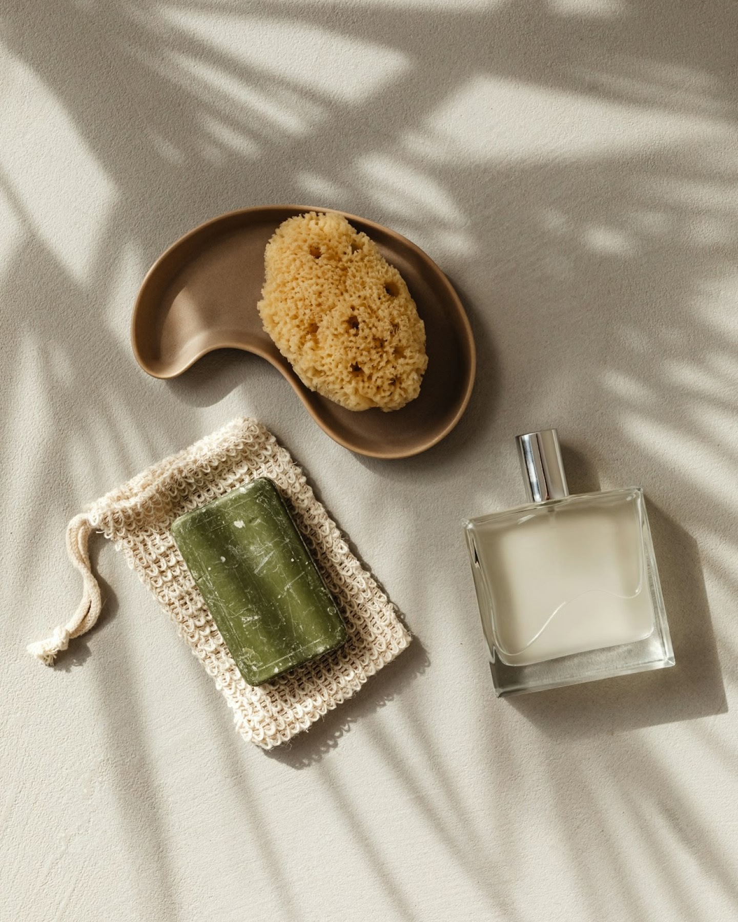 Una sábana de lino blanco con una pastilla de jabón verde, una esponja natural en un plato de madera y un frasco de perfume