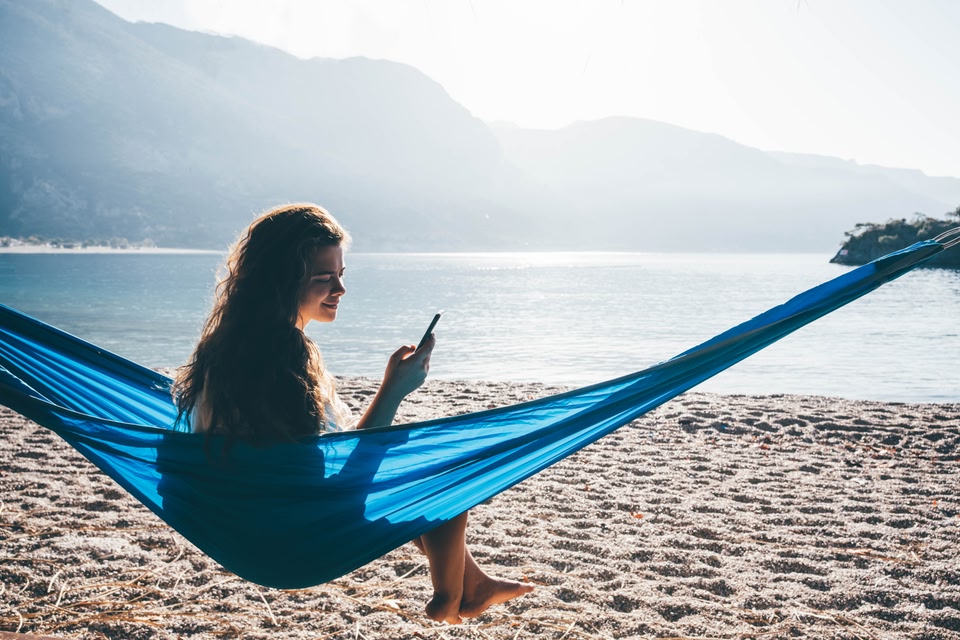 Mulher na praia sentada na rede com celular na mão verificando se Zupper é confiável