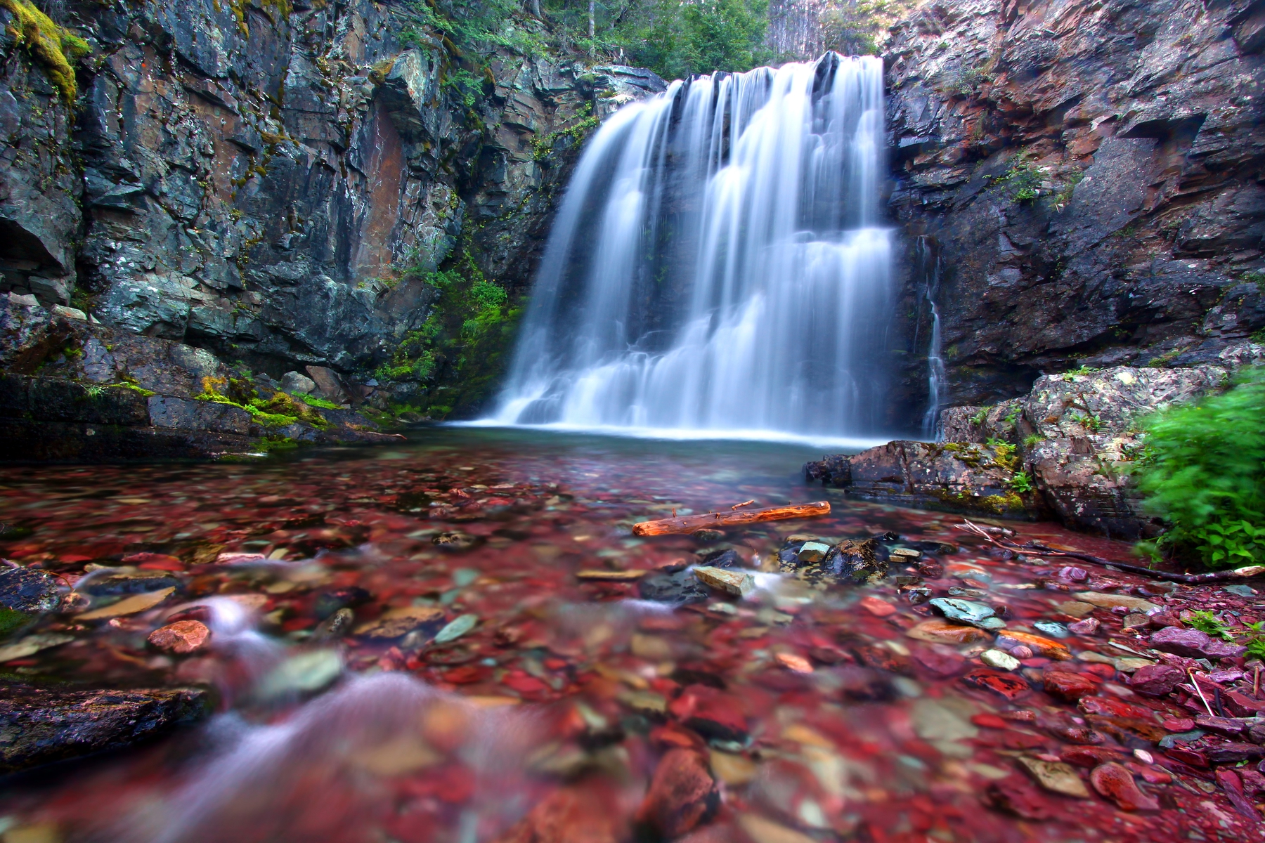 A waterfall rushing into a pond filled with red stones.