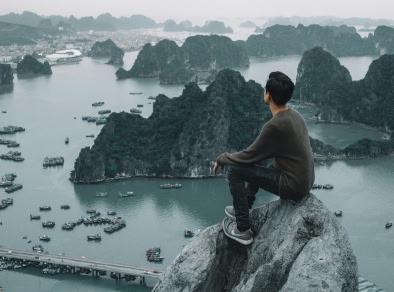 Imagen de un hombre sentado en un afloramiento rocoso con vistas a la bahía de Ha Long
