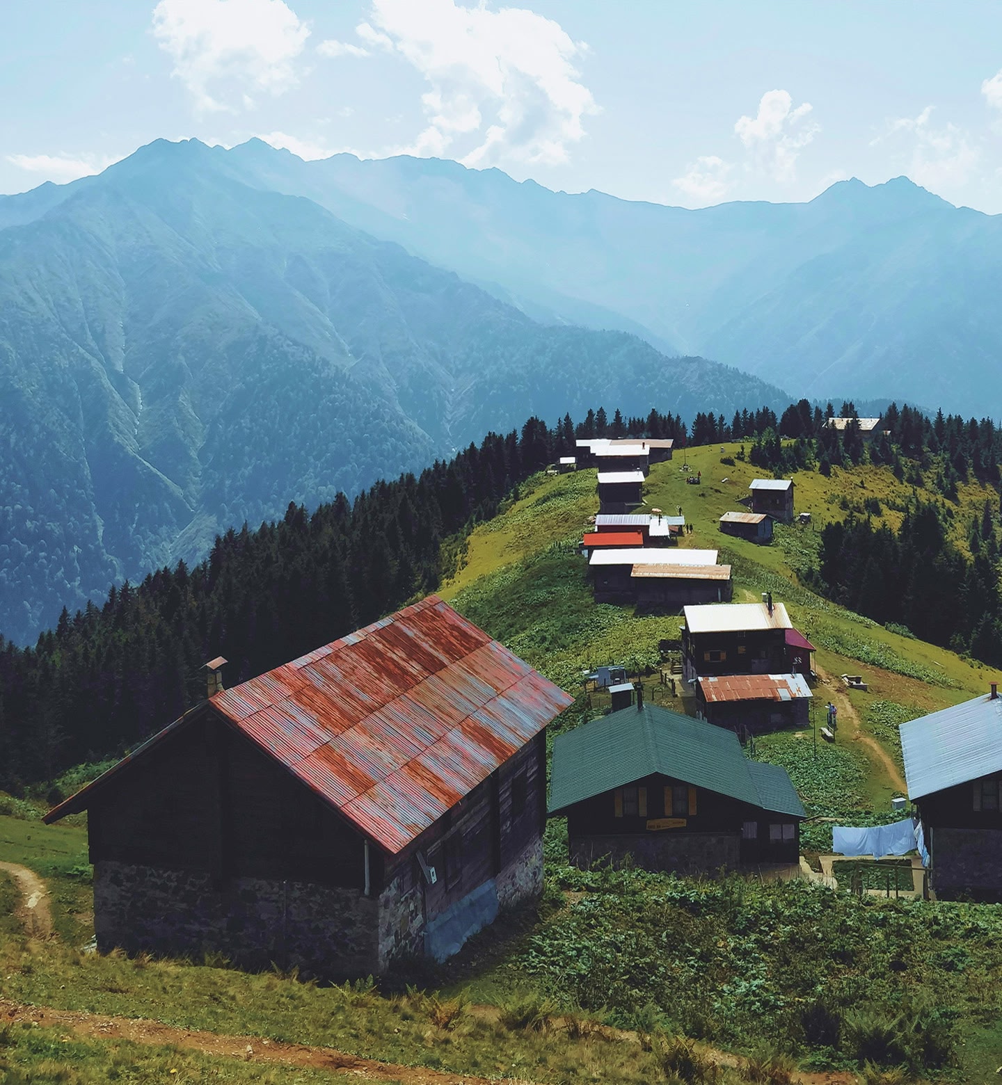 A row of mountain cabins along the top of a hill with mountains in the distance in Rize, Turkey.