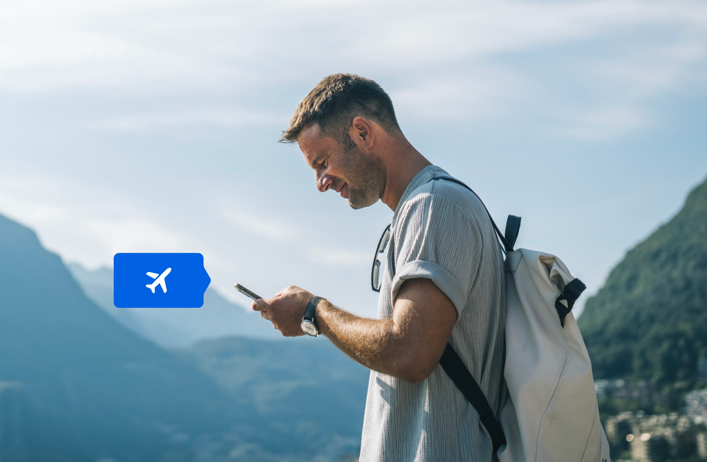 Um homem de perfil olhando para o celular na sua mão e sorrindo, escolhendo países para visitar.
