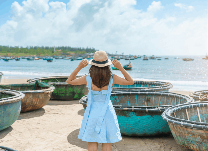 A woman on a beach in a blue dress surrounded by circular boats looking out to sea.