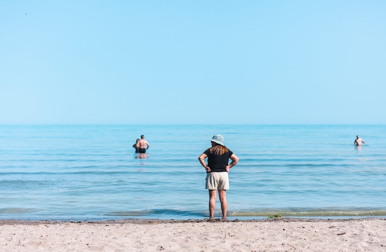woman in a bucket hat standing by the shore of Port Stanley Beach, one of the best and most popular beaches in Ontario. 