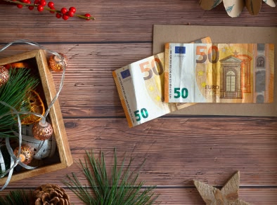 A birds eye view of table with 2 fifty euro notes, a pinecone and a wooden box with fairy lights