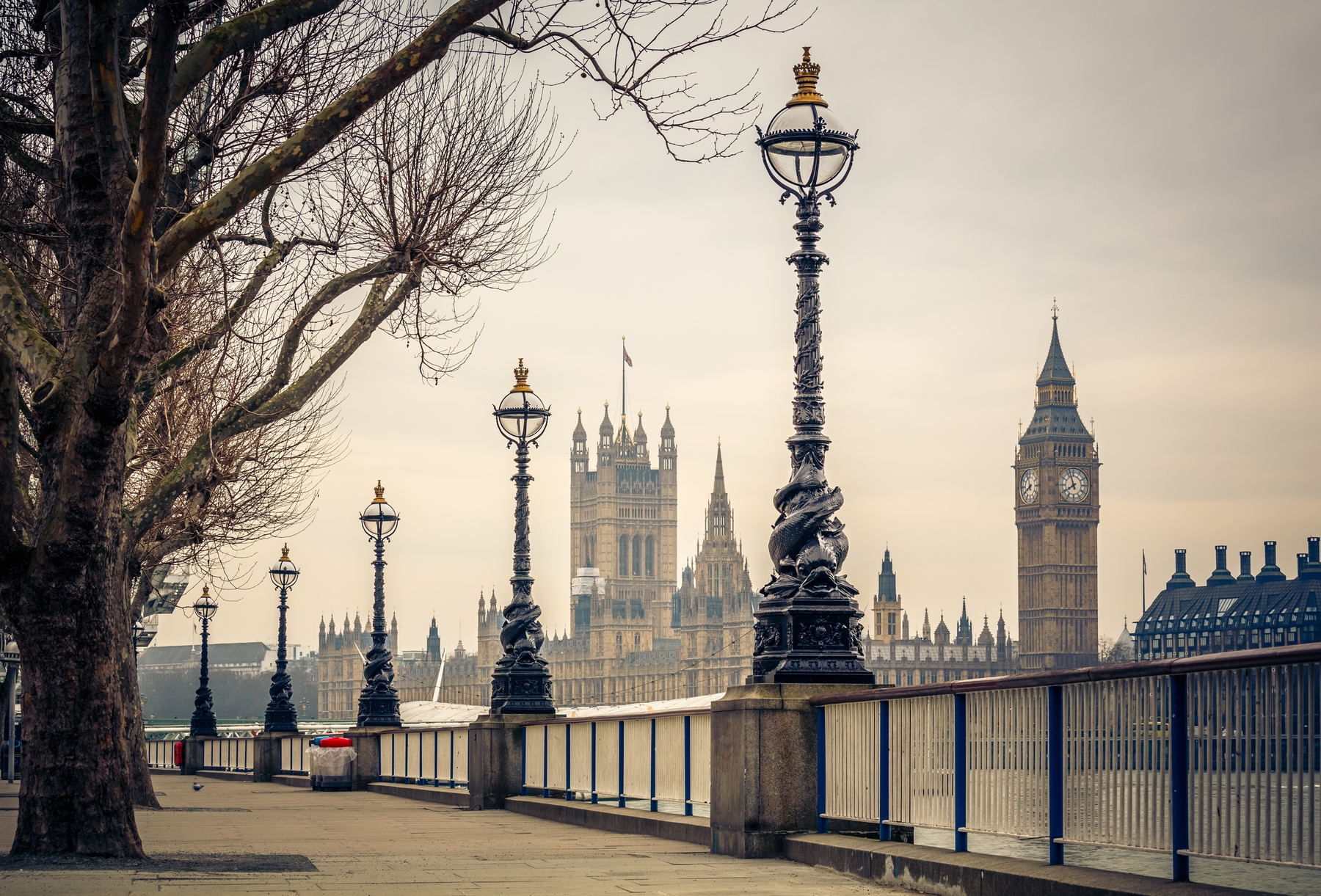 The South Bank on a foggy day, featuring the famous dolphin lampposts in the foreground and Big Ben and the Houses of Parliament in the background.
