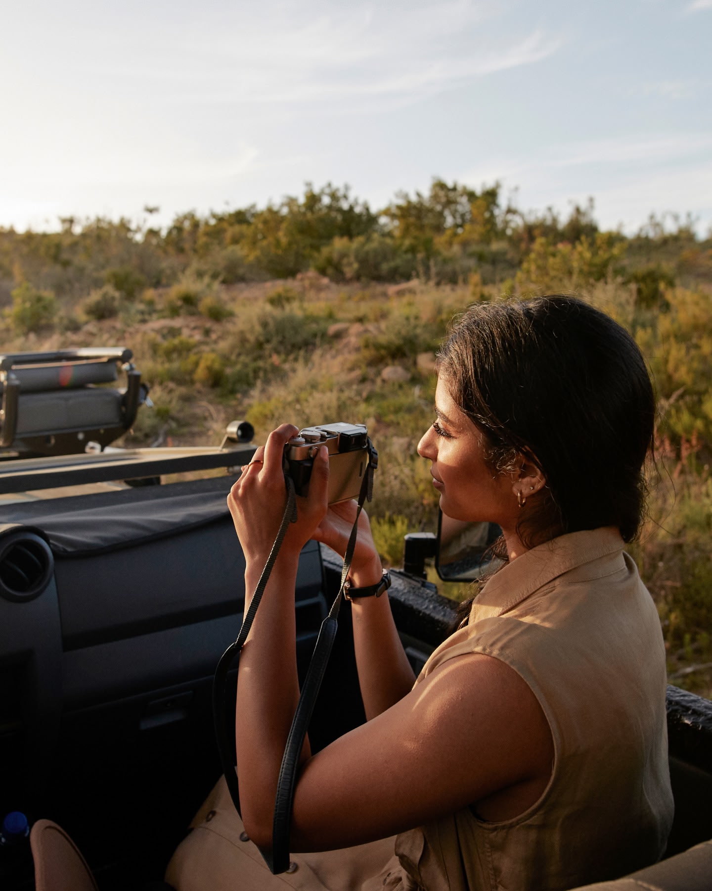A woman sitting in the back of an open air jeep, looking through a camera lens.