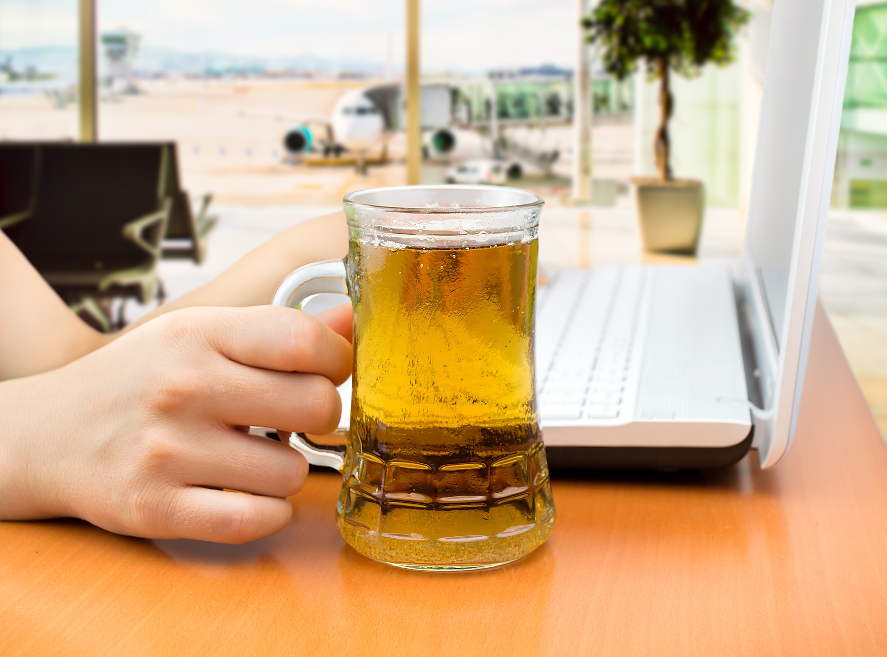person holding a glass of beer and watching tv on their laptop at the airport. list of airport hacks for travel.