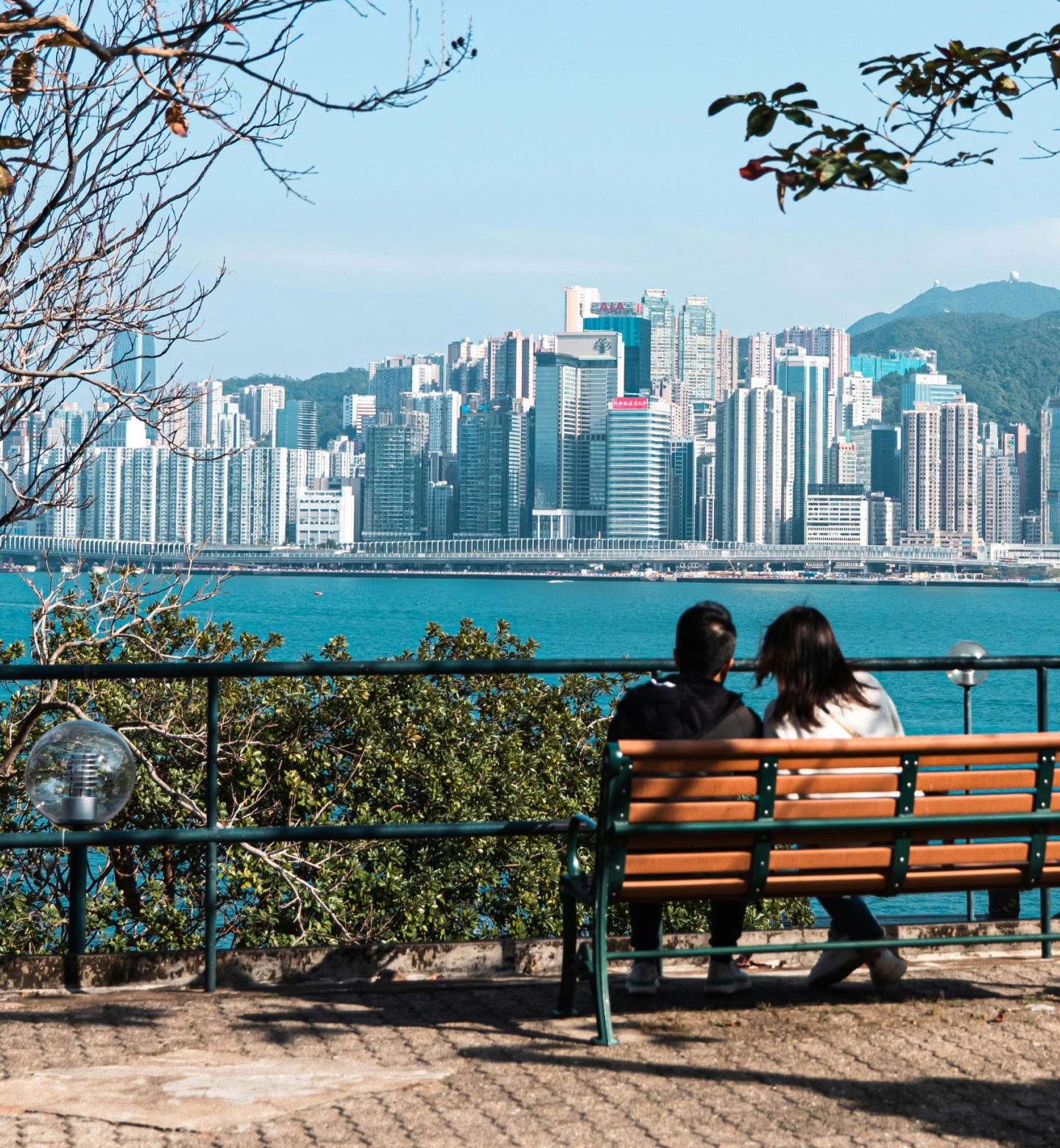 Two people sit facing the harbour and Hong Kong’s towering skyline.