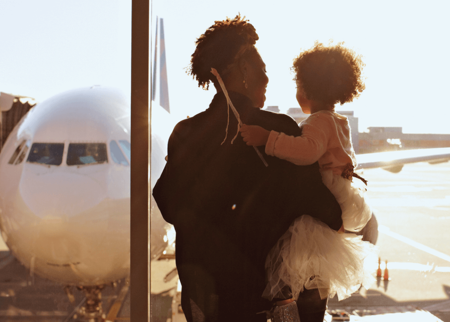 Adult holding a child looking out the window at an airport.