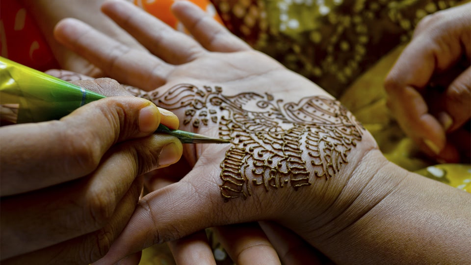 someone drawing henna on the palm of a hand