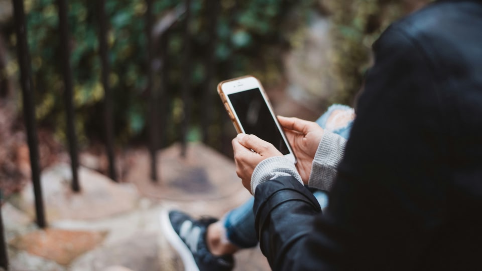 pessoa sentada em uma escada olhando no celular, utilizando app para calcular custos de viagem