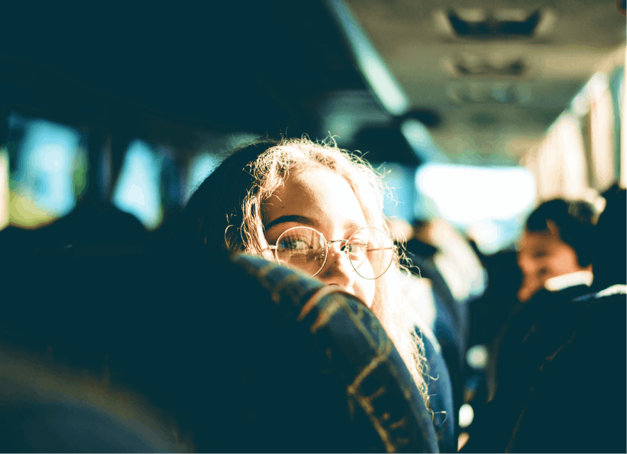 A woman looking over her shoulder on a bus. Part of her face is obscured by her seat. 