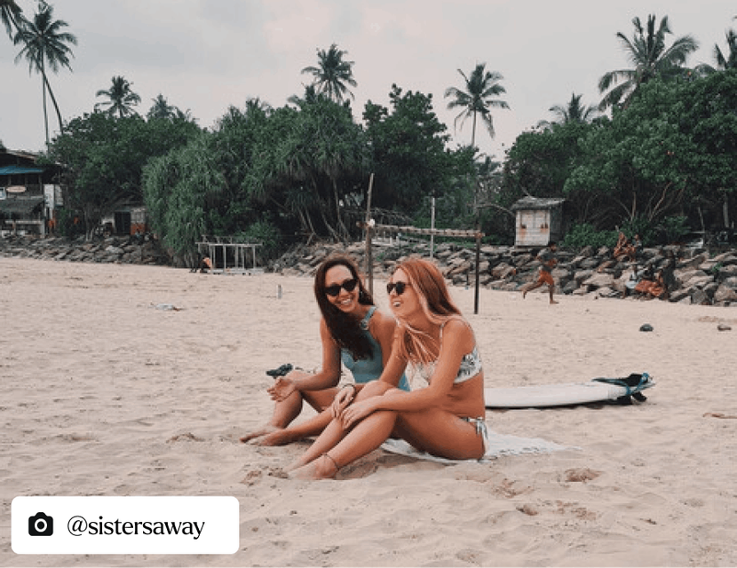 Two women sat on a beach laughing and enjoying each others company