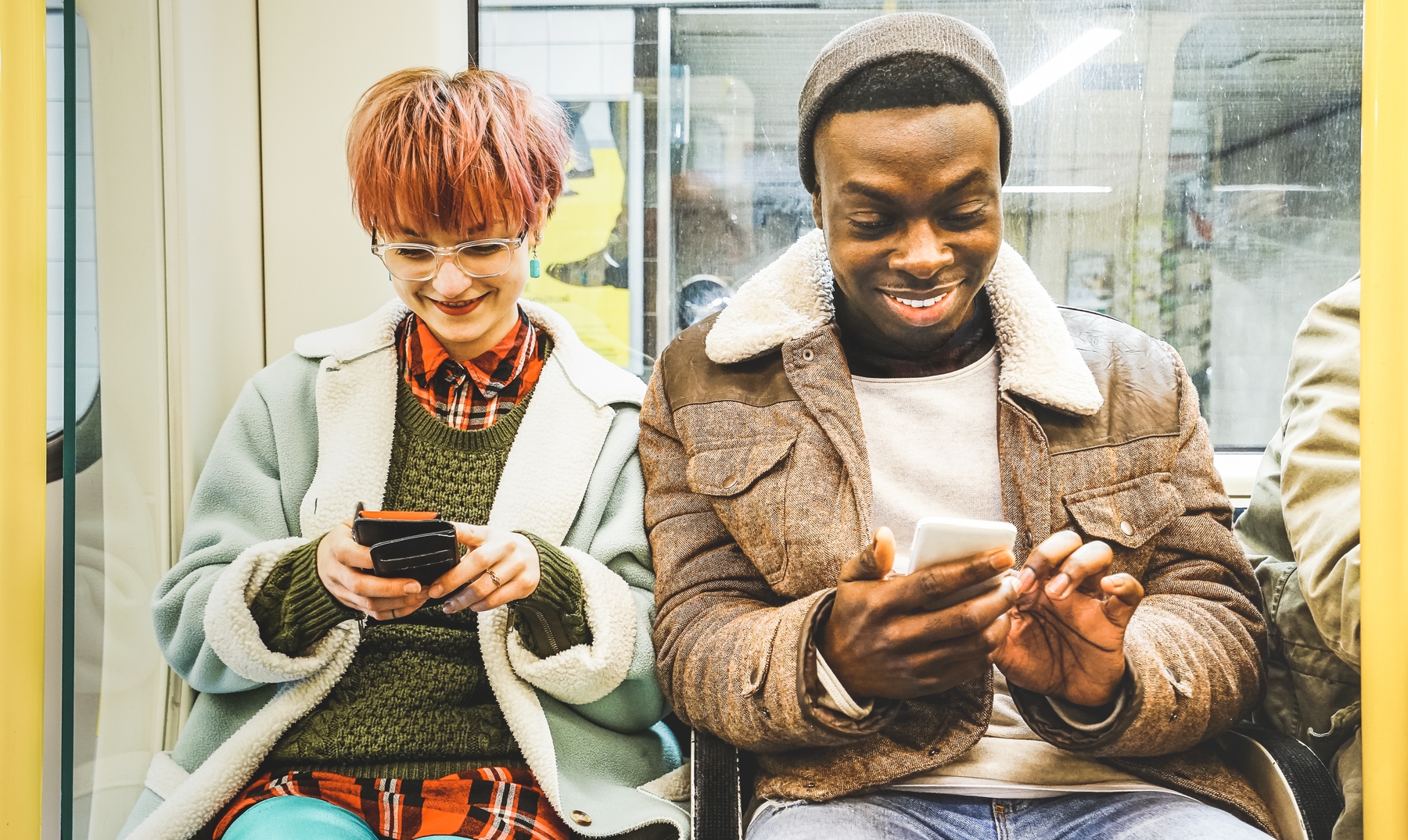 Multiracial hipster friends couple having fun with smartphone in subway train - Urban relationship concept with young people watching mobile phone in city underground area - Bright desaturated filter