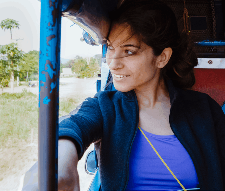 Joyful woman passenger seated in the back of a tuk-tuk, wearing a warm smile as she appreciates the scenic view