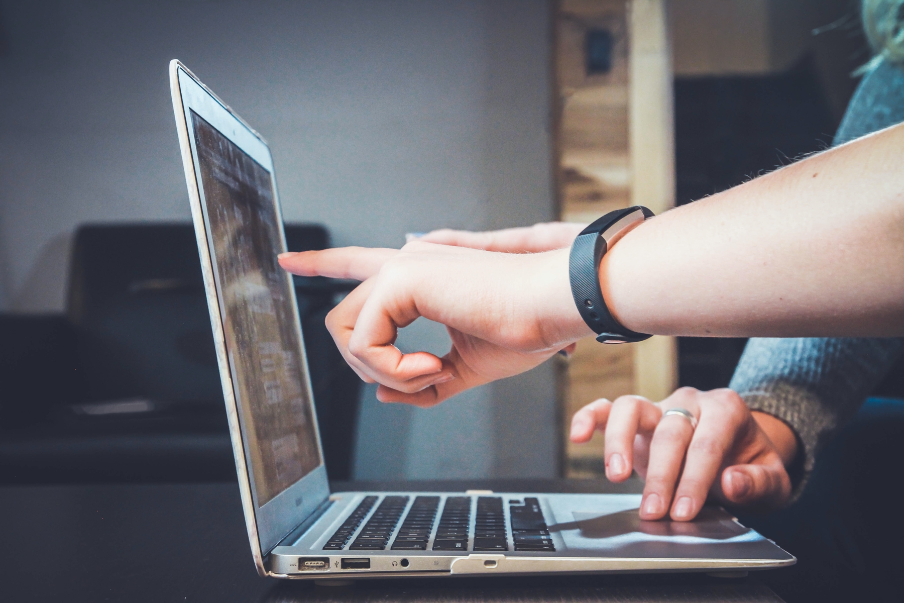 Multiple hands are pointing at a computer screen.