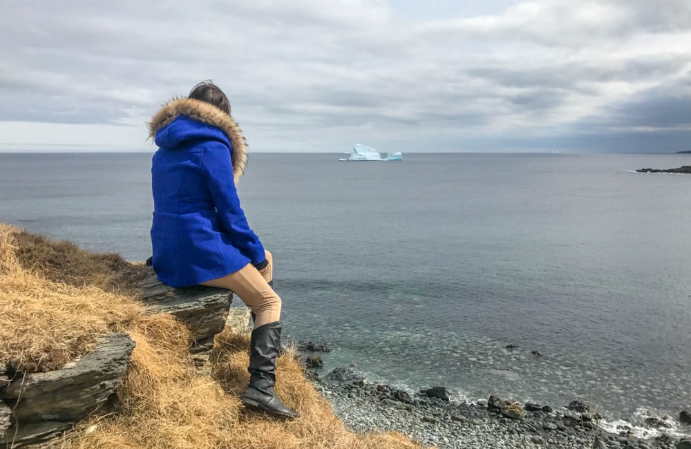 Blogger Lora sitting on a rock by the coastline of Newfoundland in Iceberg Alley, a dream destination in Canada