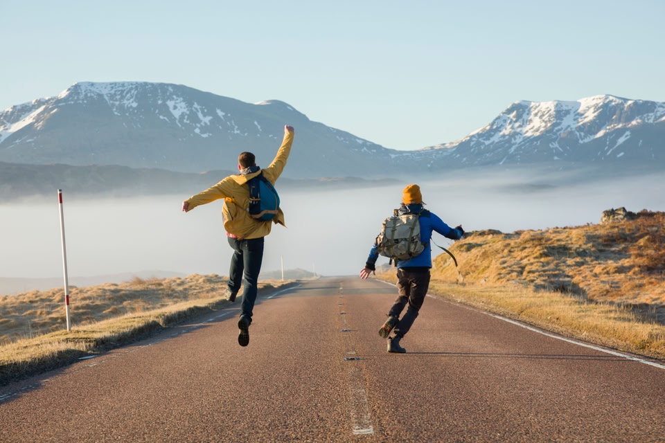 Rear view of two men jumping with joy on a country road in Glencoe, Scottish Highlands.
