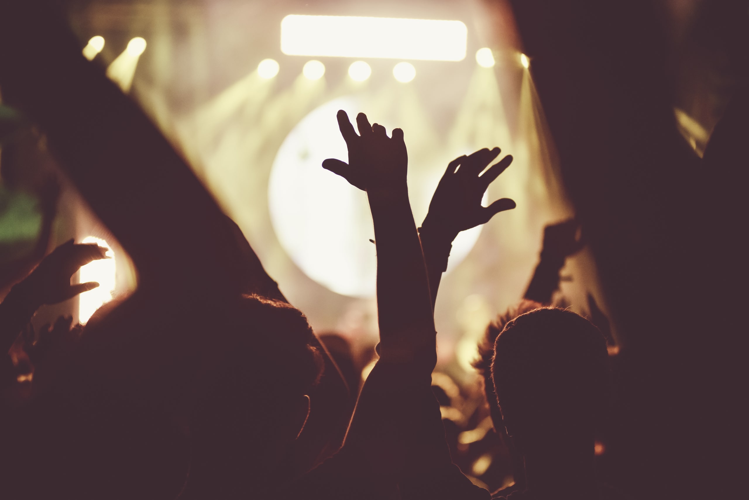 Crowd of audience with hands raised at a music festival. Lights streaming down from above the stage. best music festivals in the USA 2024.