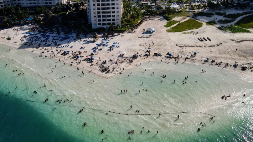 Vista aérea de pessoas na praia de areia branca e mar azul em Cancún durante o dia.